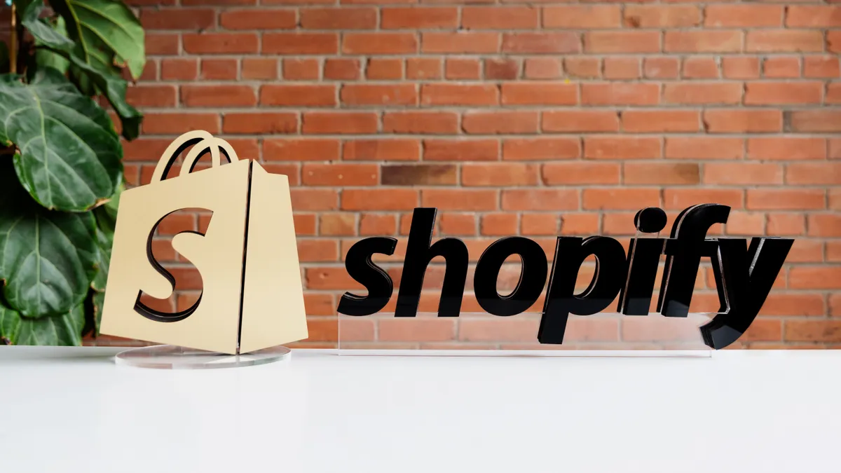 Shopify bag logo and name. in front of a brick wall.