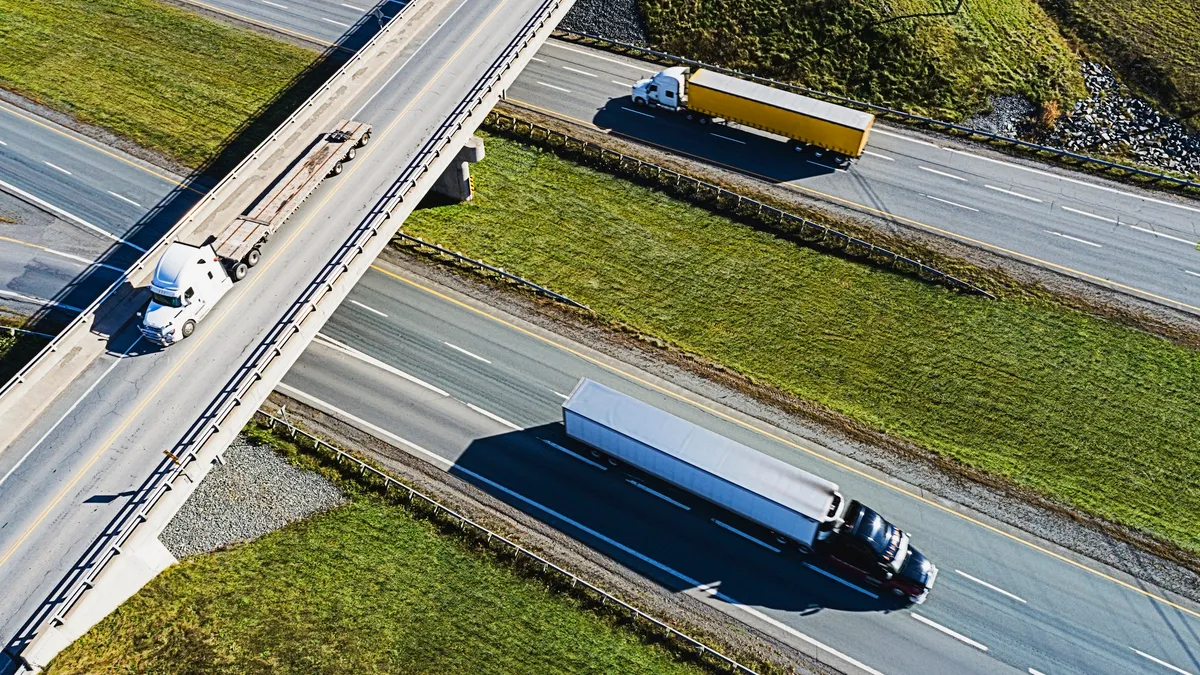 Trucks drive above and below a highway overpass.