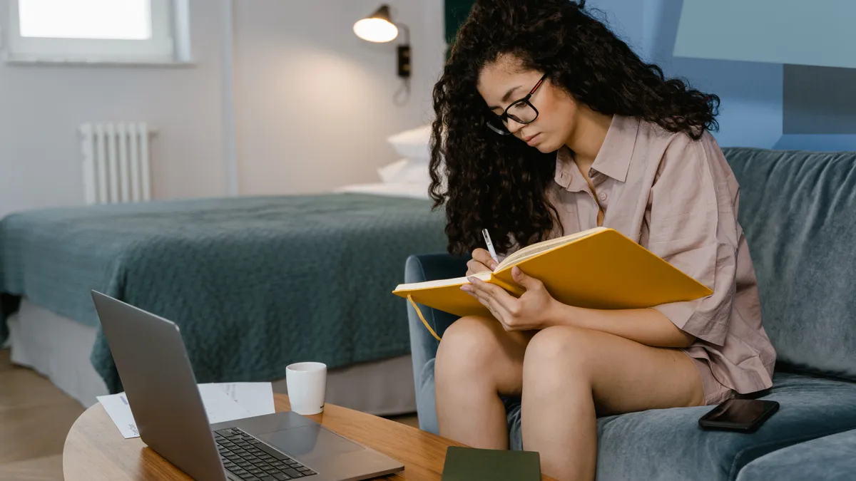 A young woman writes in a notebook on the couch