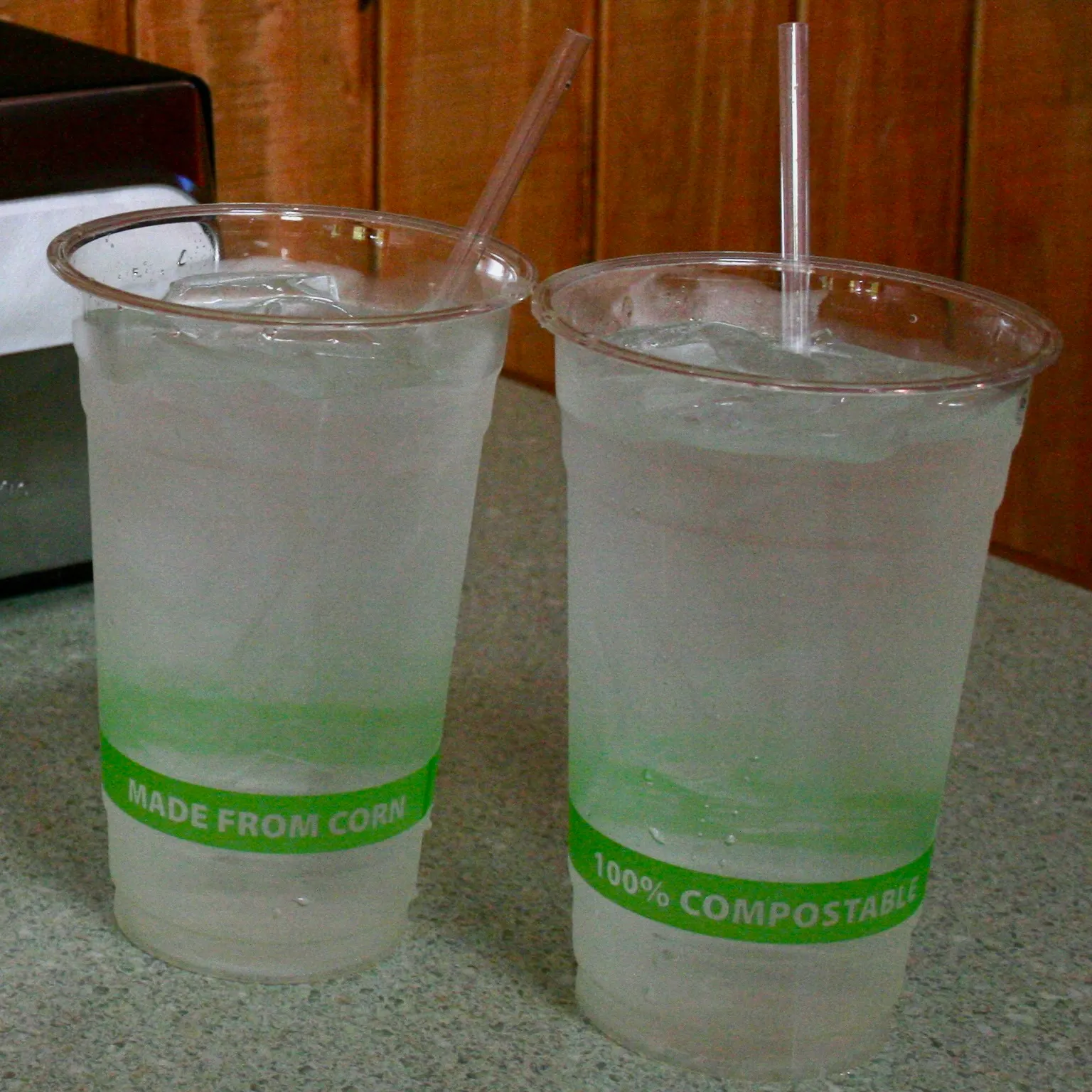 Two corn-based plastic cups, labeled compostable, sit on a table with straws sticking out