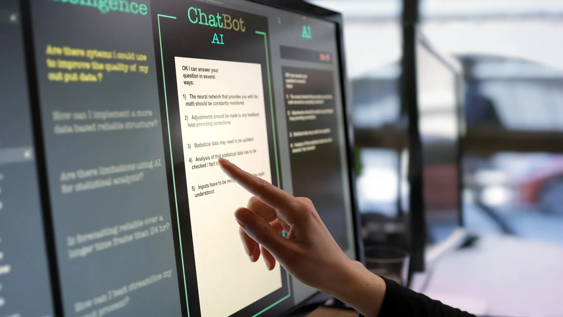 Close-up stock photograph showing a touchscreen monitor on which a woman’s hand is asking an AI chatbot pre-typed questions.