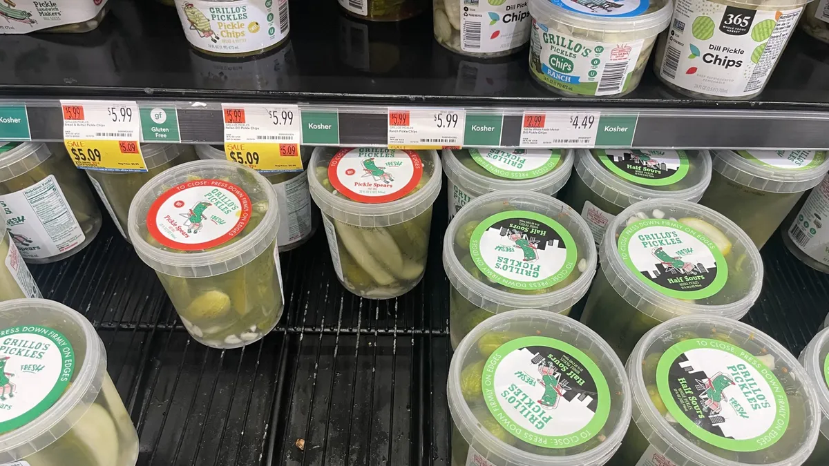 Plastic Grillo's Pickles tubs in a grocery store display case