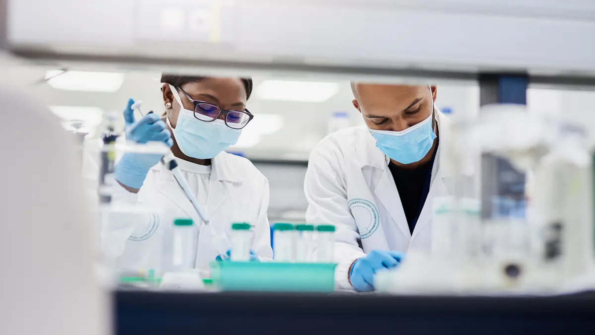 Two people in white coats work at a laboratory bench.