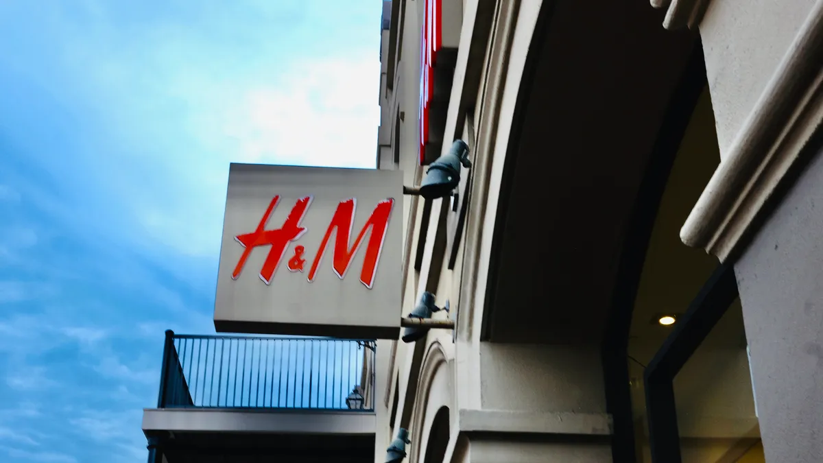 An "H&M" sign with red letters juts out from a building against a dramatic blue sky.