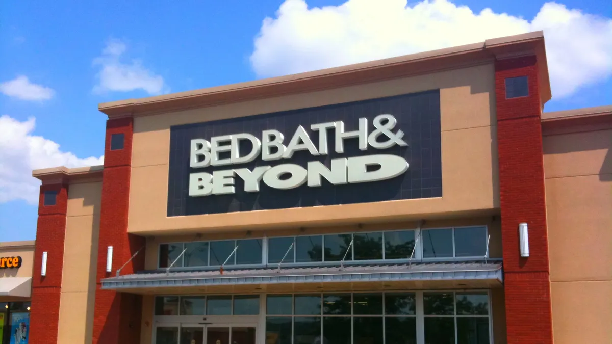 Puffy white clouds in a bright blue sky, behind a red-trimmed storefront that reads "Bed Bath & Beyond."