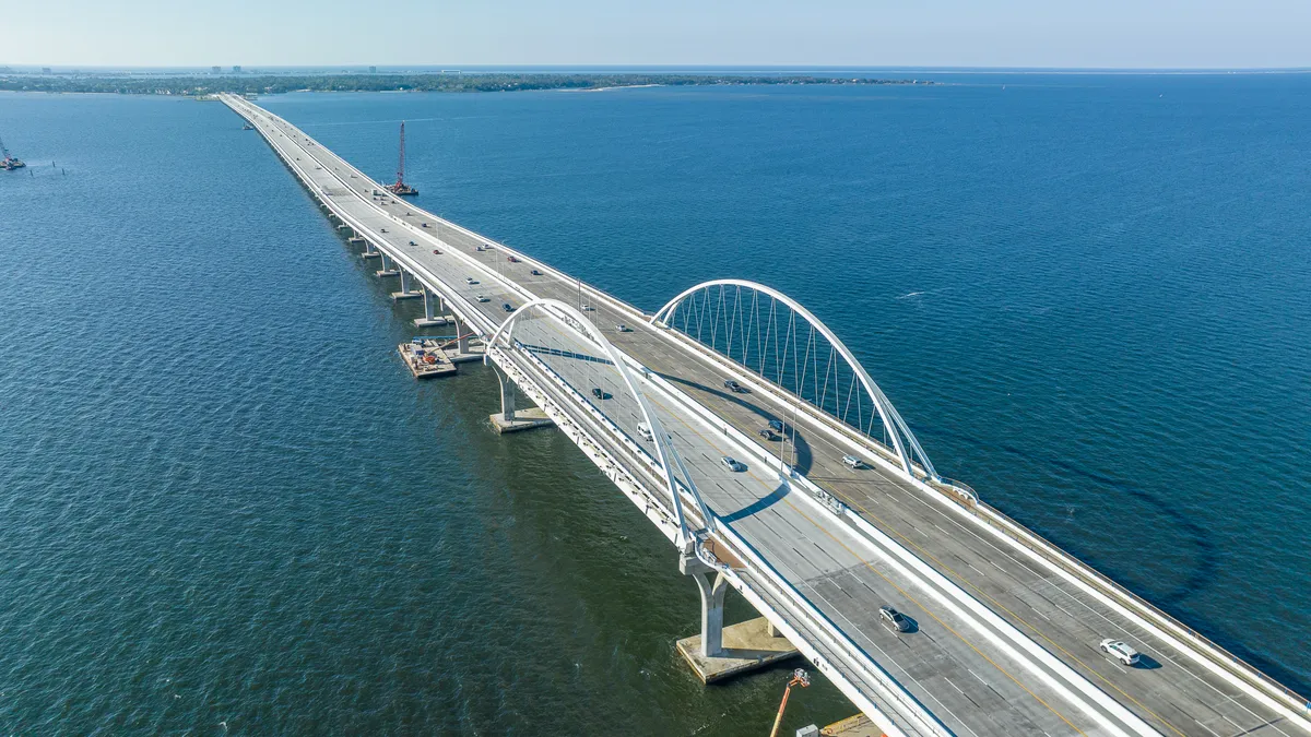 Aerial view of a double bridge with six lanes, spanning bright blue water.