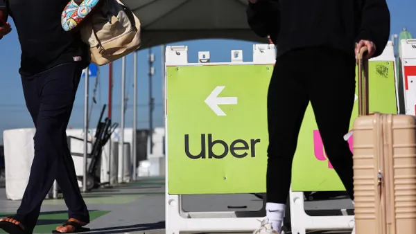 Two people wearing black seen from the wait down walk by a sign with an arrow and the word "Uber."