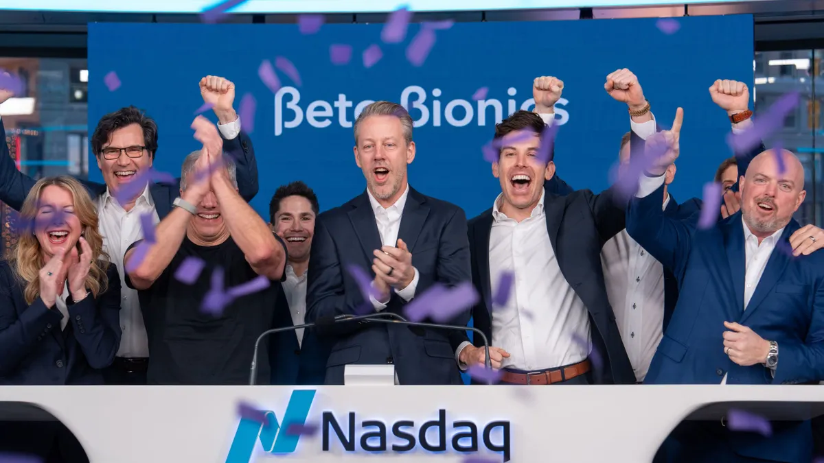 A group of people cheering inside the Nasdaq building, standing behind a podium.