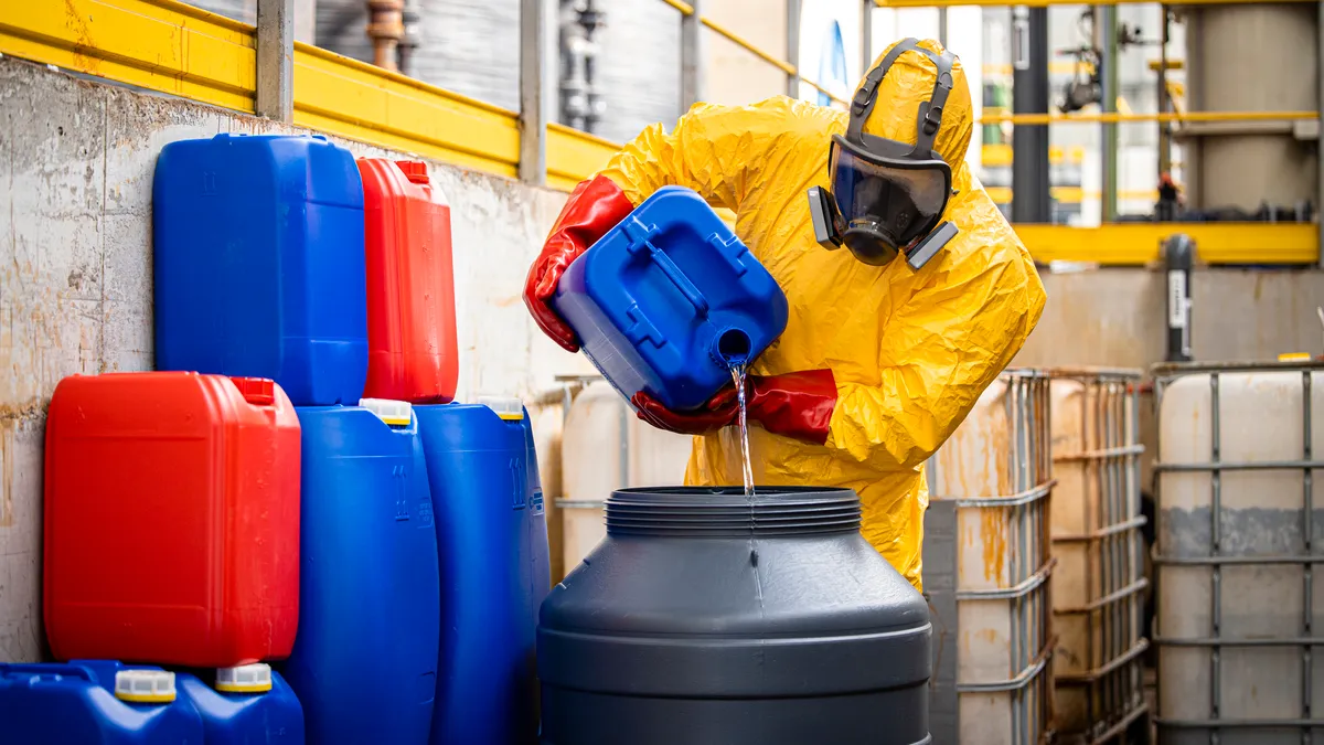 Chemical worker or technologist in yellow protection suit and gas mask making sulfuric acid for industry.