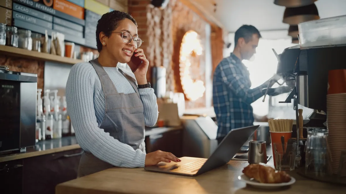 Small business owner talks on phone while standing at register