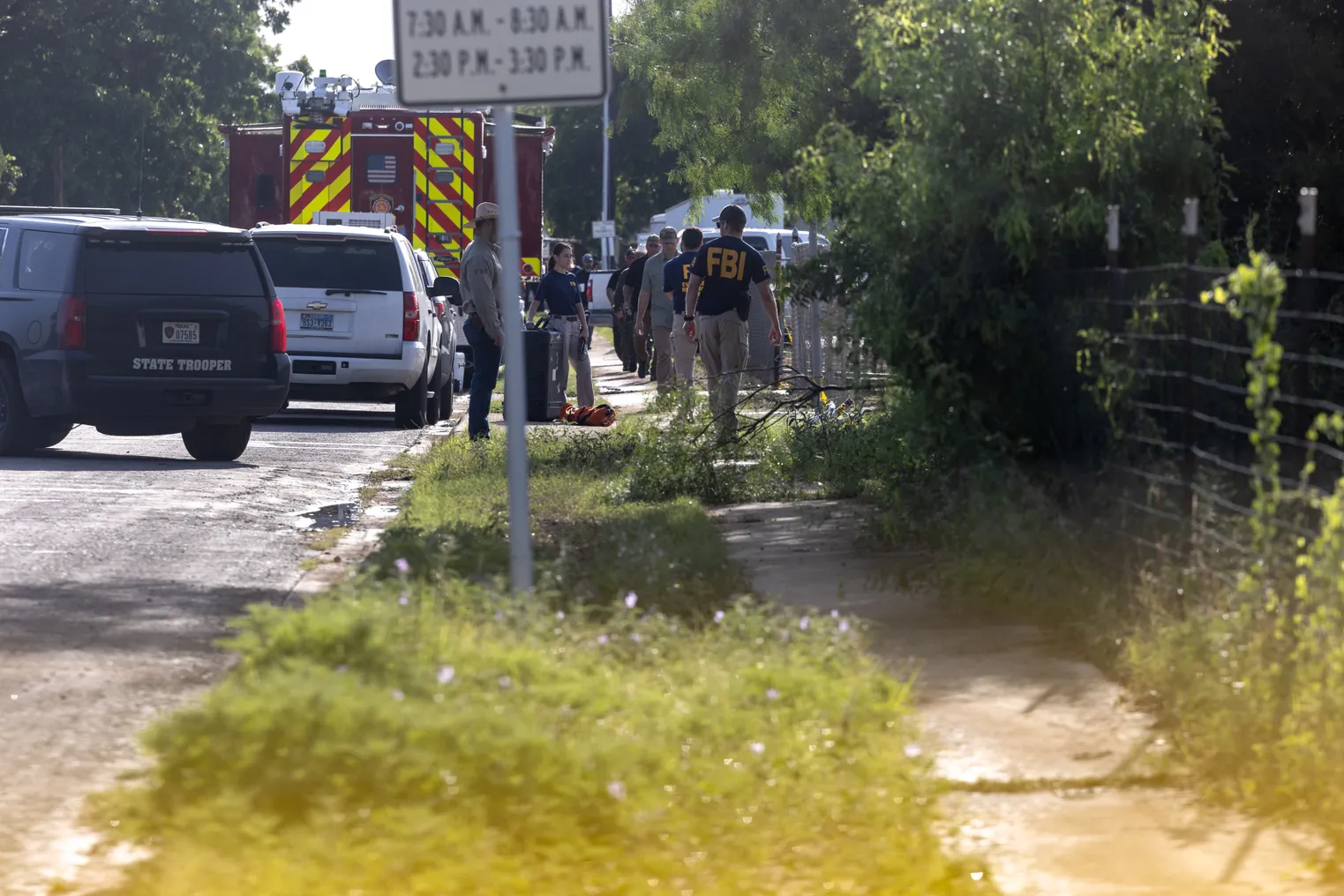 first responders walk on a side walk with vehicles to their left