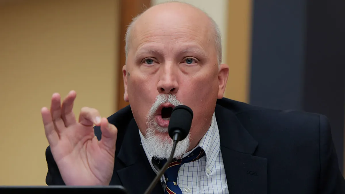 A person in a suit speaks into a microphone with their mouth open