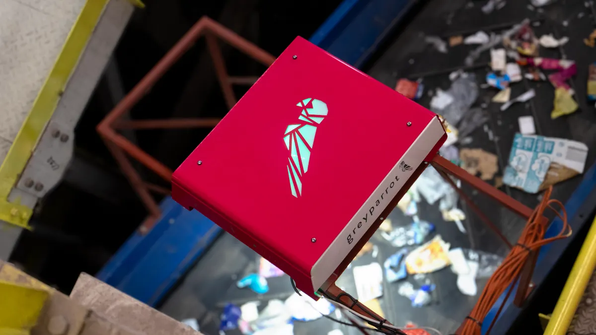 An electronic device positioned over collected recyclable materials on a conveyor belt.