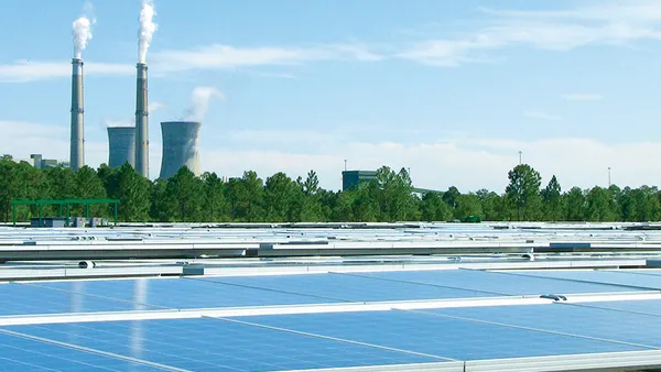 A power plant sits behind an array of solar panels.