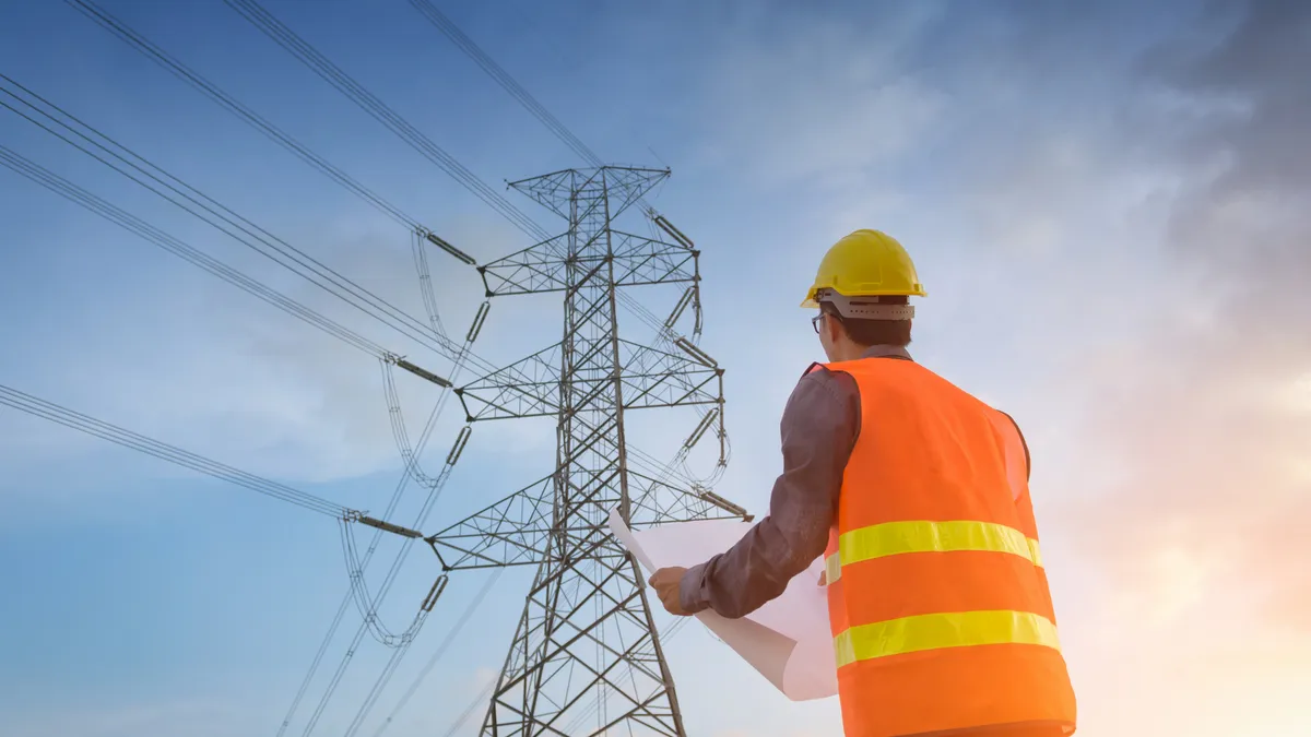 Engineering working on a high-voltage tower and checking the information on paper at sunset background.