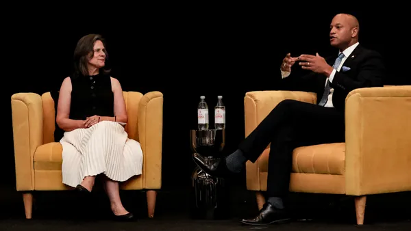 Two people sit across from each other on a stage.