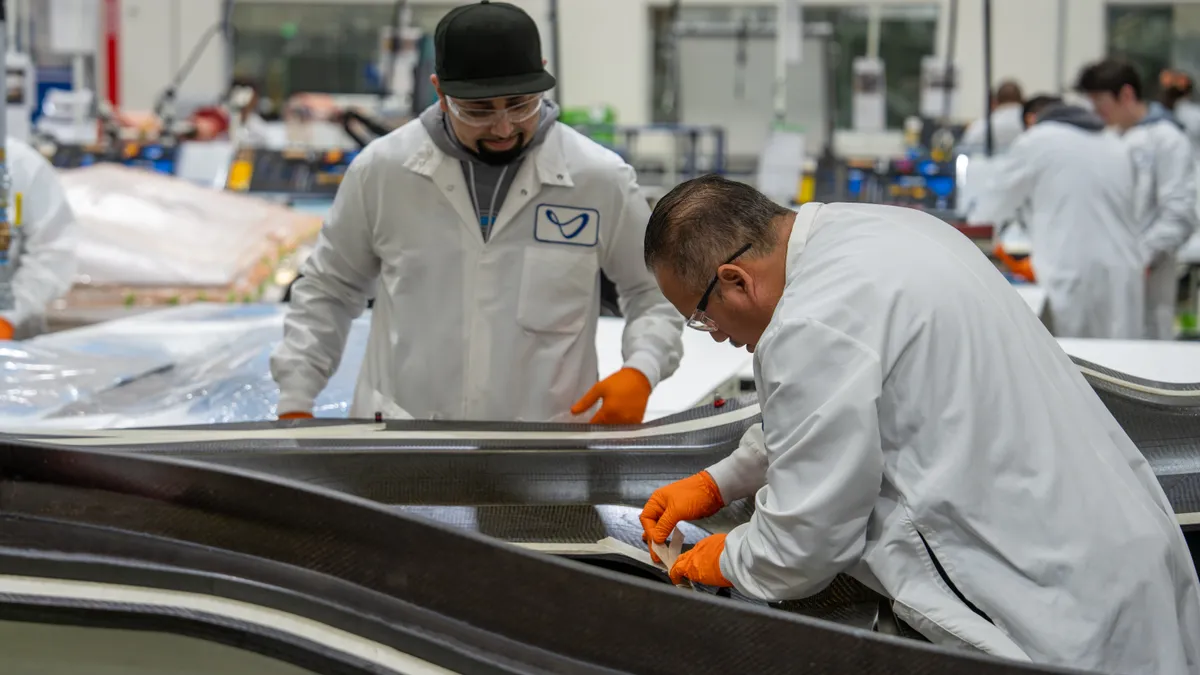 Two people wearing protective goggles and white protective coats in a factory.