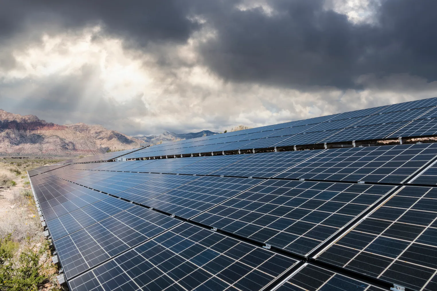 Solar panels in a desert with storm clouds in the background.