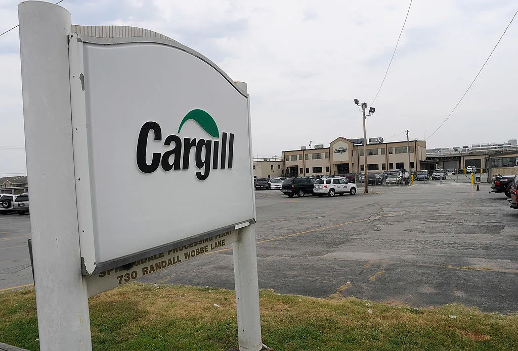 A sign reading "Cargill" is seen at the entrance of a parking lot to a factory building