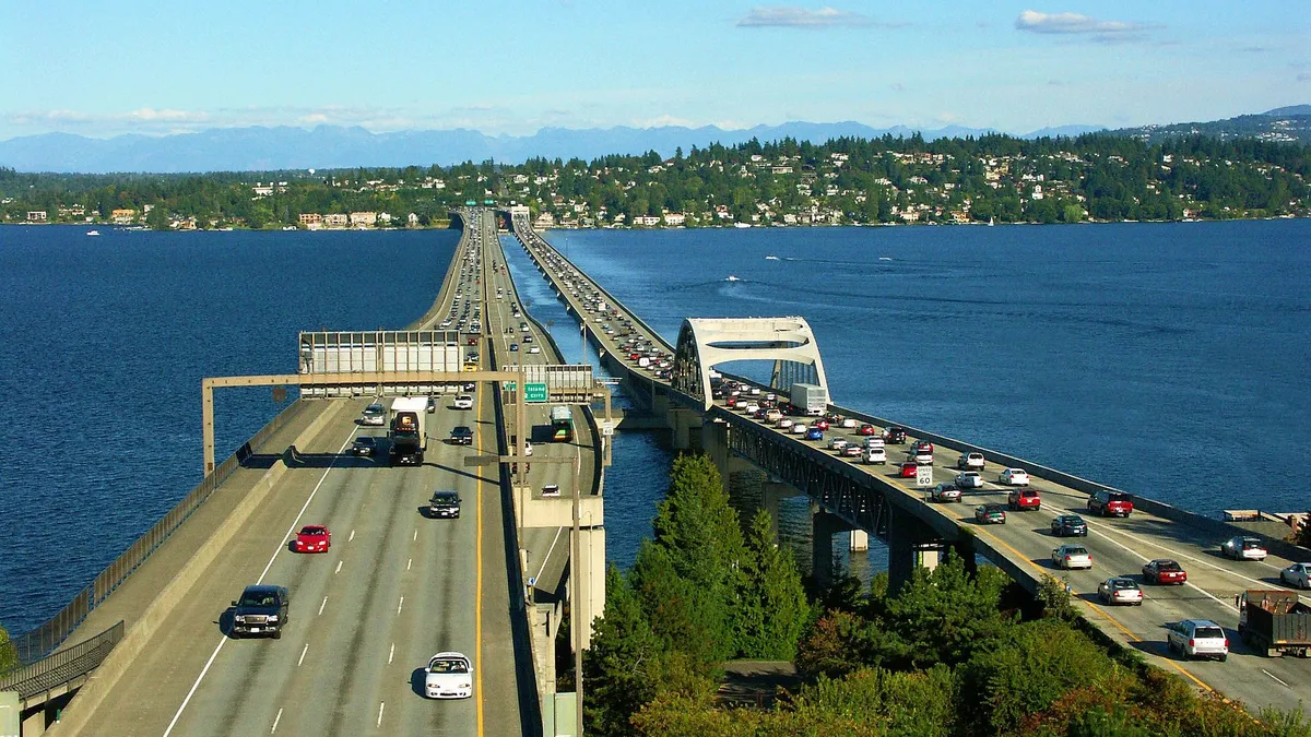 Twin multi-lane, open bridges filled with cars span a bright blue body of water.