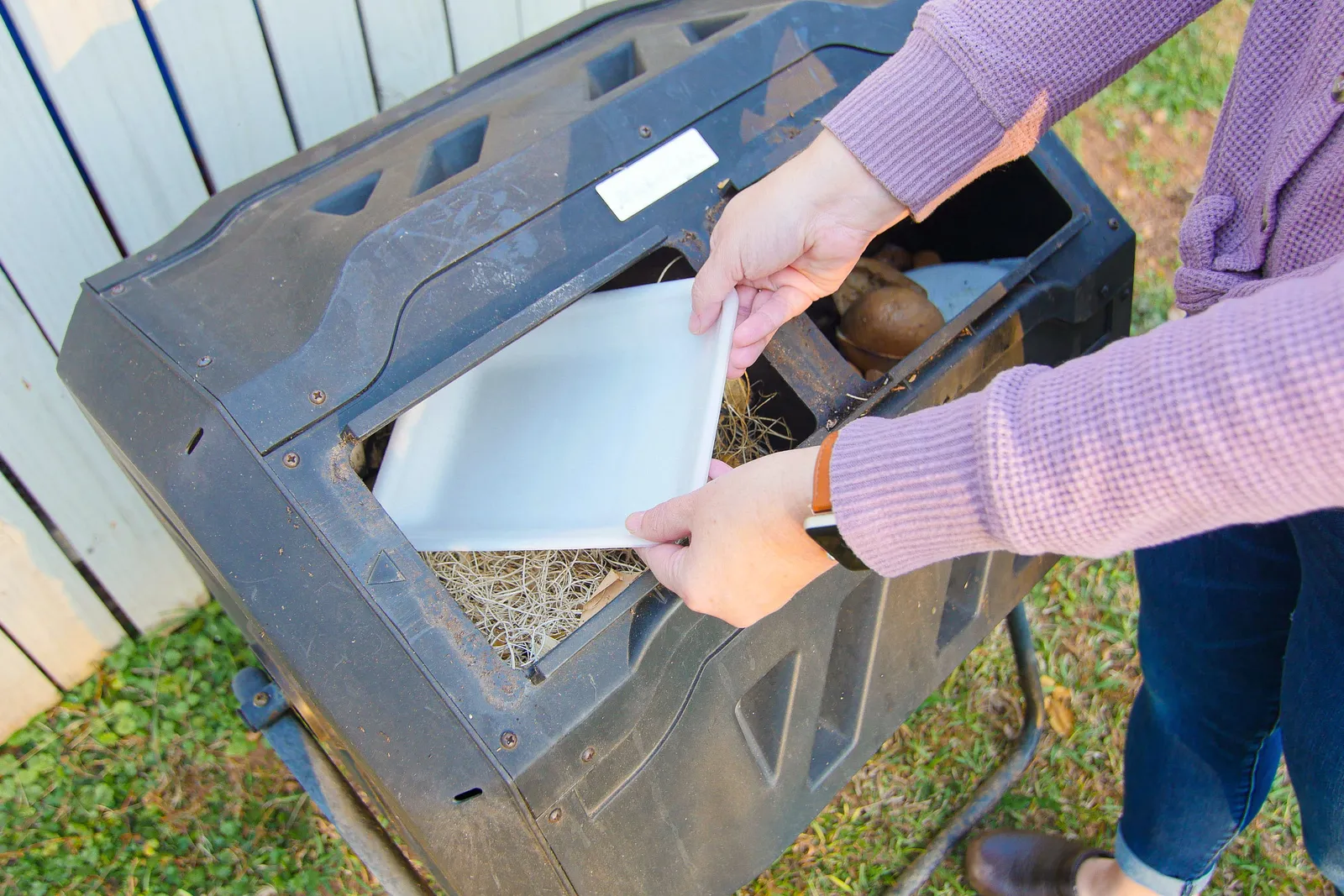 A person&#x27;s hands place a Cryovac compostable tray into a home compost unit.