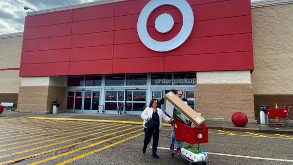 Two people walking out from a store with a cart full of items.