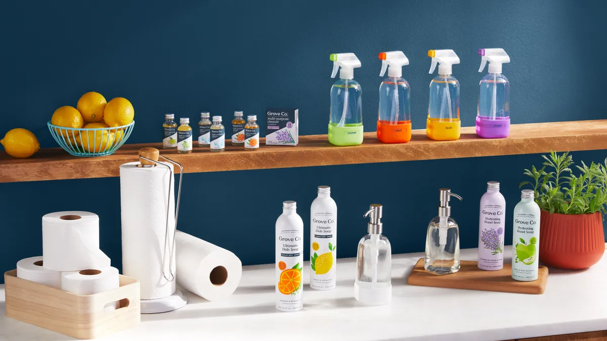 Green shelves with clear and colorful cleaning bottles next to paper towel rolls