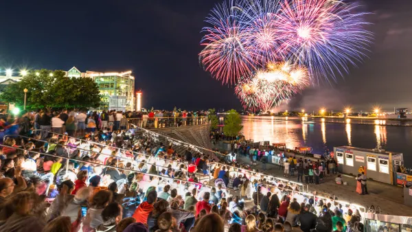 Fireworks exploding over a body of water while a crowd watches from the stands.