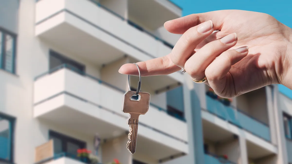 hand holding keys in front of apartment building