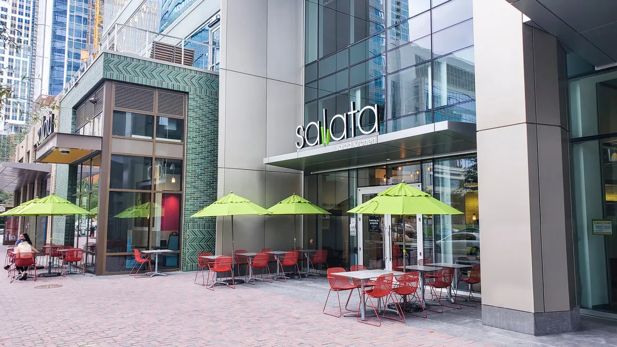 An exterior shot of a Salata store. It's a restaurant with some green umbrellas in front.