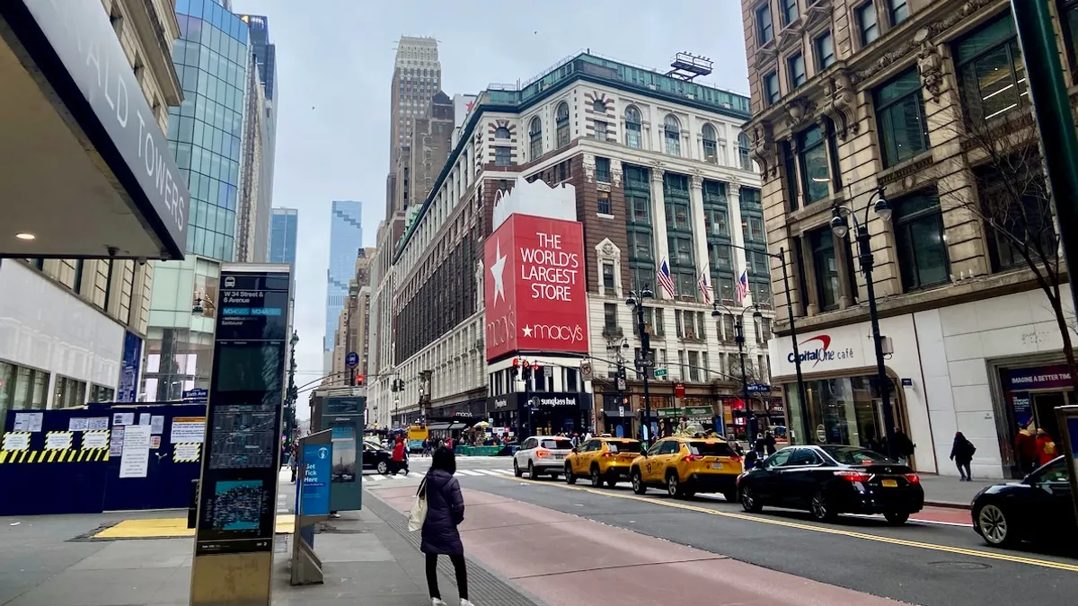 A large department store building seen down the block, with a person seen standing in the foreground.