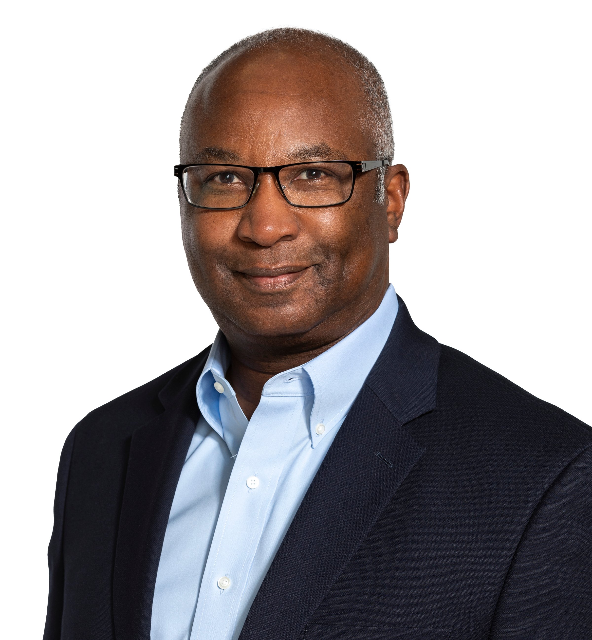 A person in a suit wearing glasses smiles faintly.