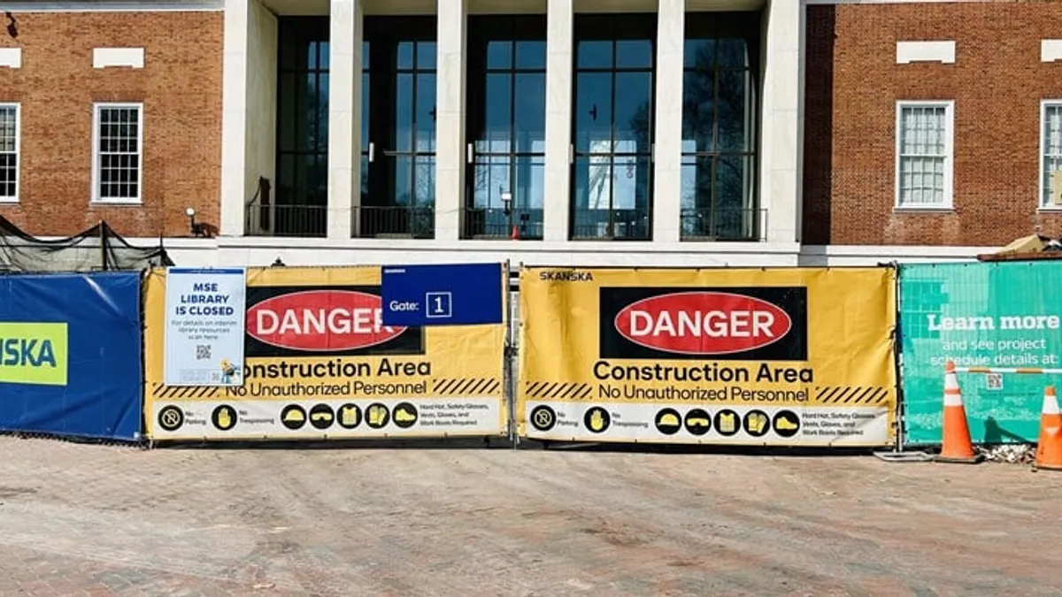 Construction hazard signs on a fence surrounding a jobsite.