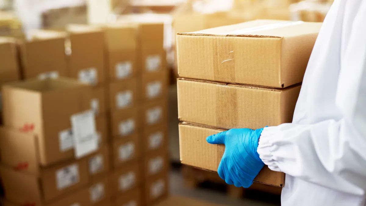 Close-up of worker in sterile gear carrying a box.