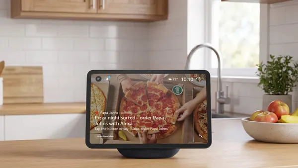 An Amazon Echo Show device on a kitchen counter displays an ad from Papa Johns.