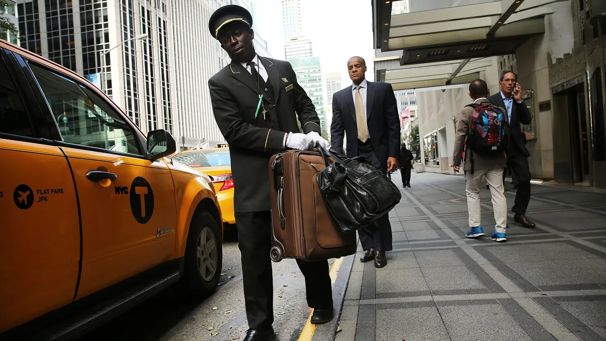 An employee carries a guest's bag to his taxi.