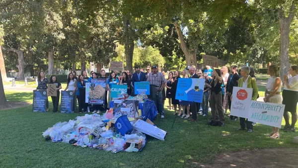 a group of people hold signs behind a pile of discarded plastic