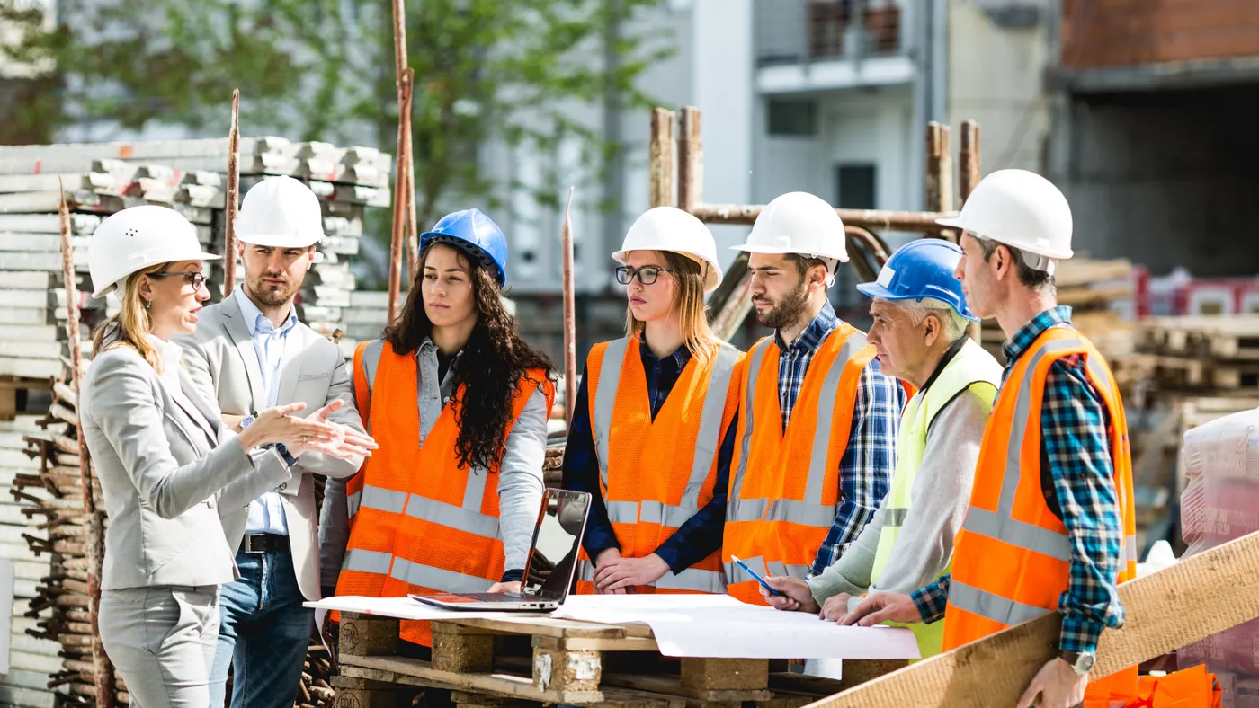 A group of construction workers stand around on a jobsite having a meeting.
