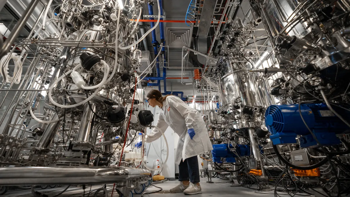 A person in lab safety gear bends slightly and works with one of Future Meat Technologies' large silver bioreactors.