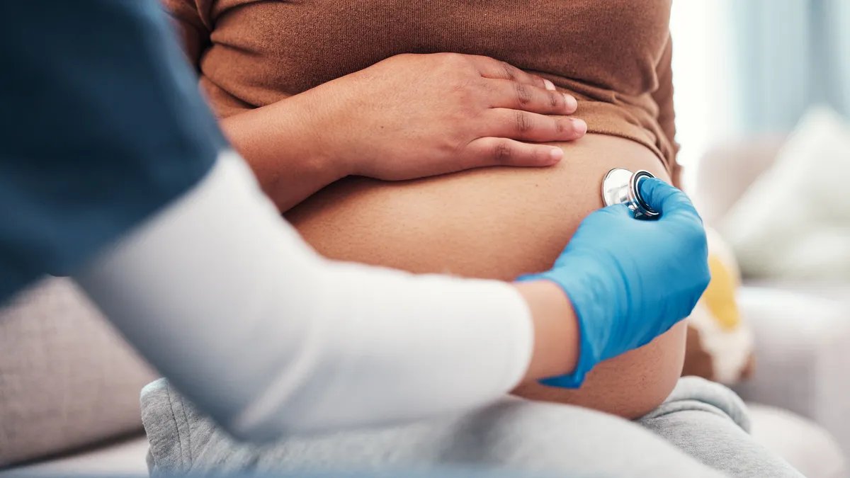 A pregnant person is checked with a stethoscope in a doctor's office.