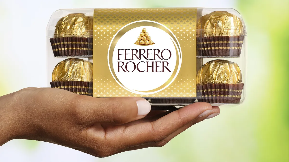 A person's hand holding a box of individually wrapped Ferrero Rocher chocolates.