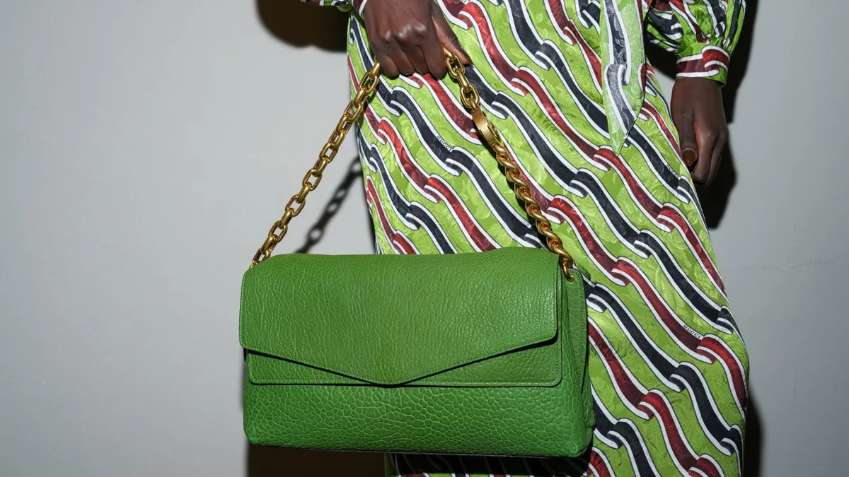 A model in a striped dress holds a lime handbag on a gold chain.
