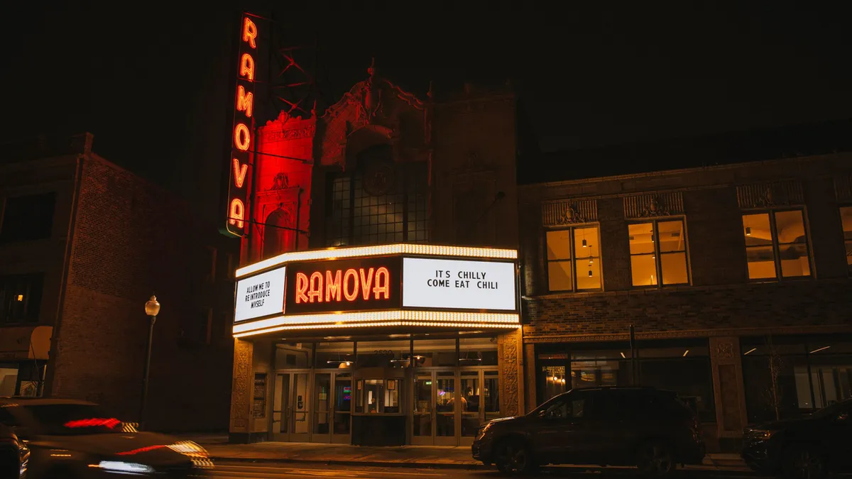 The front of a theater lights up in the darkness. The red contrasts with the colors of a city at night.