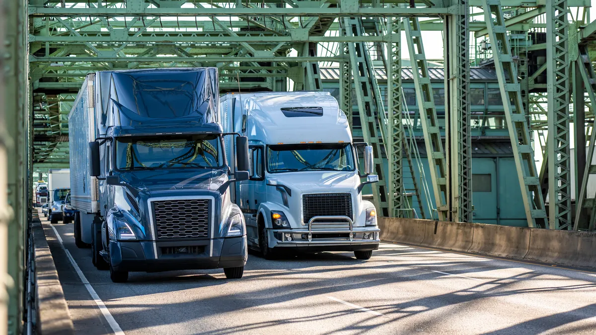 Trucks and passenger vehicles cross a bridge under metal trusses.