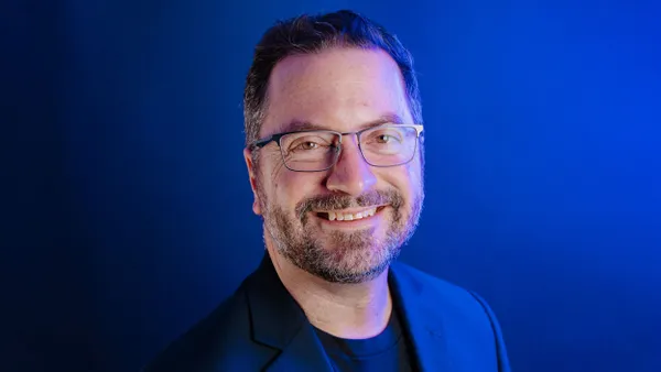 An image of a man with a beard and glasses in front of a dark blue background