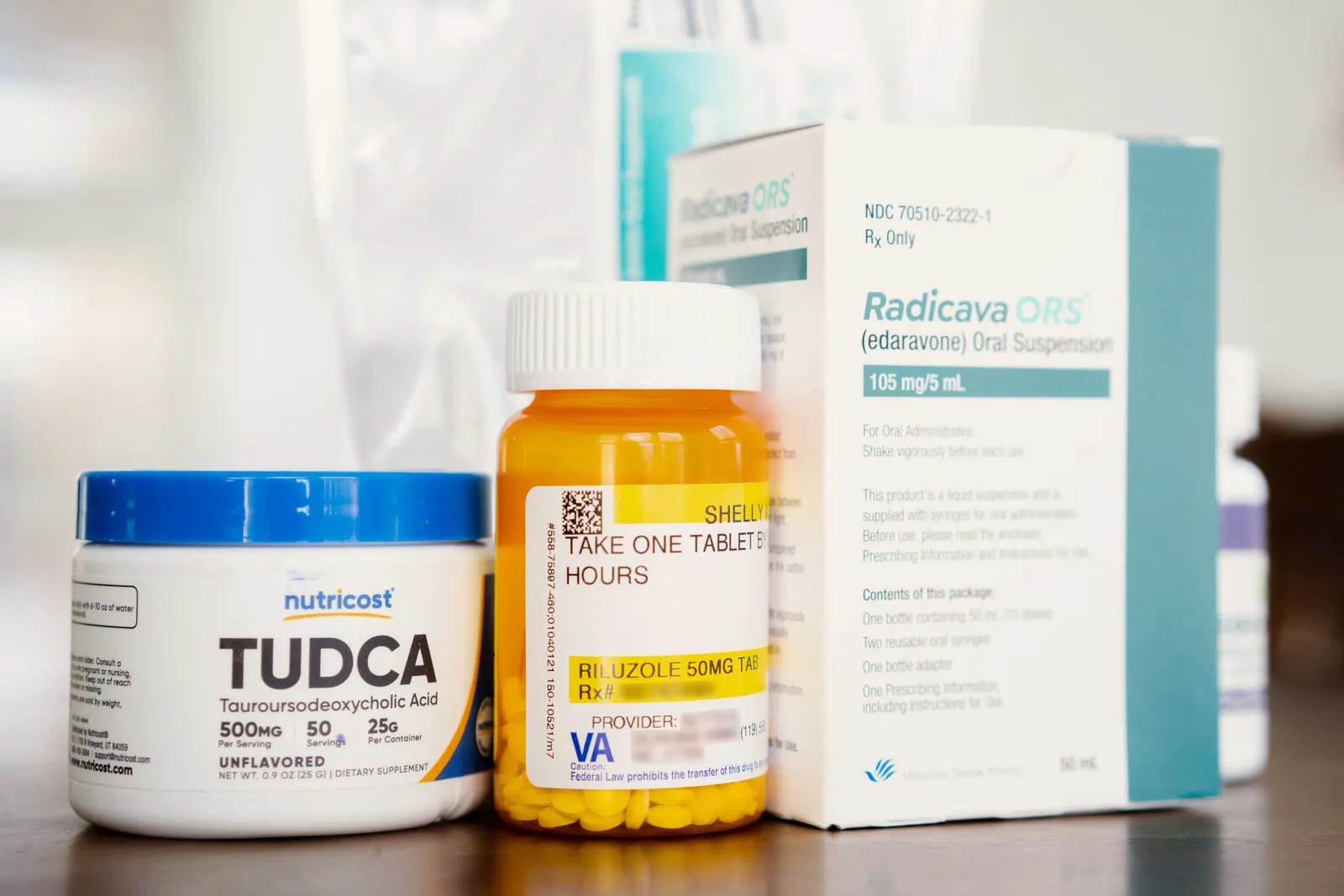 A row of prescriptions on a counter; the bottles read "Tudca, Riluzole, Radicava Ors."