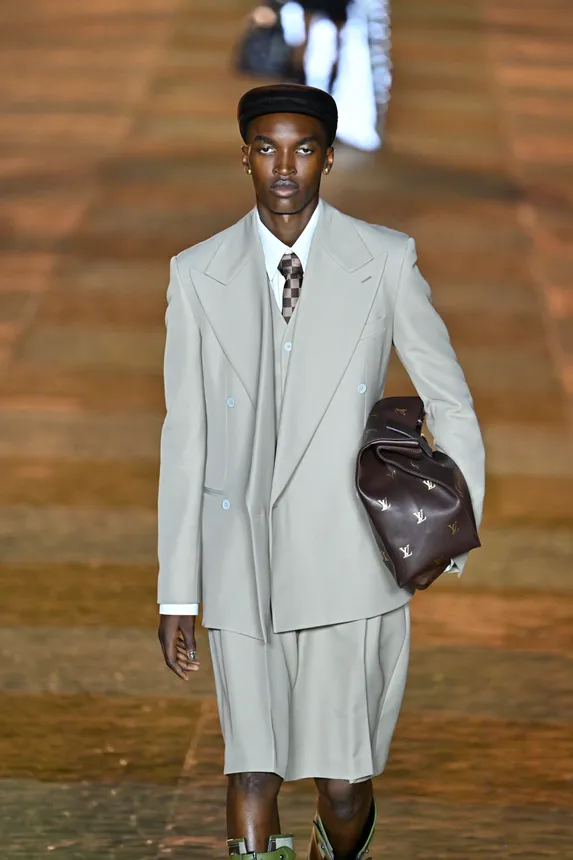 A man in a gray shorts suit walks down a fashion runway.