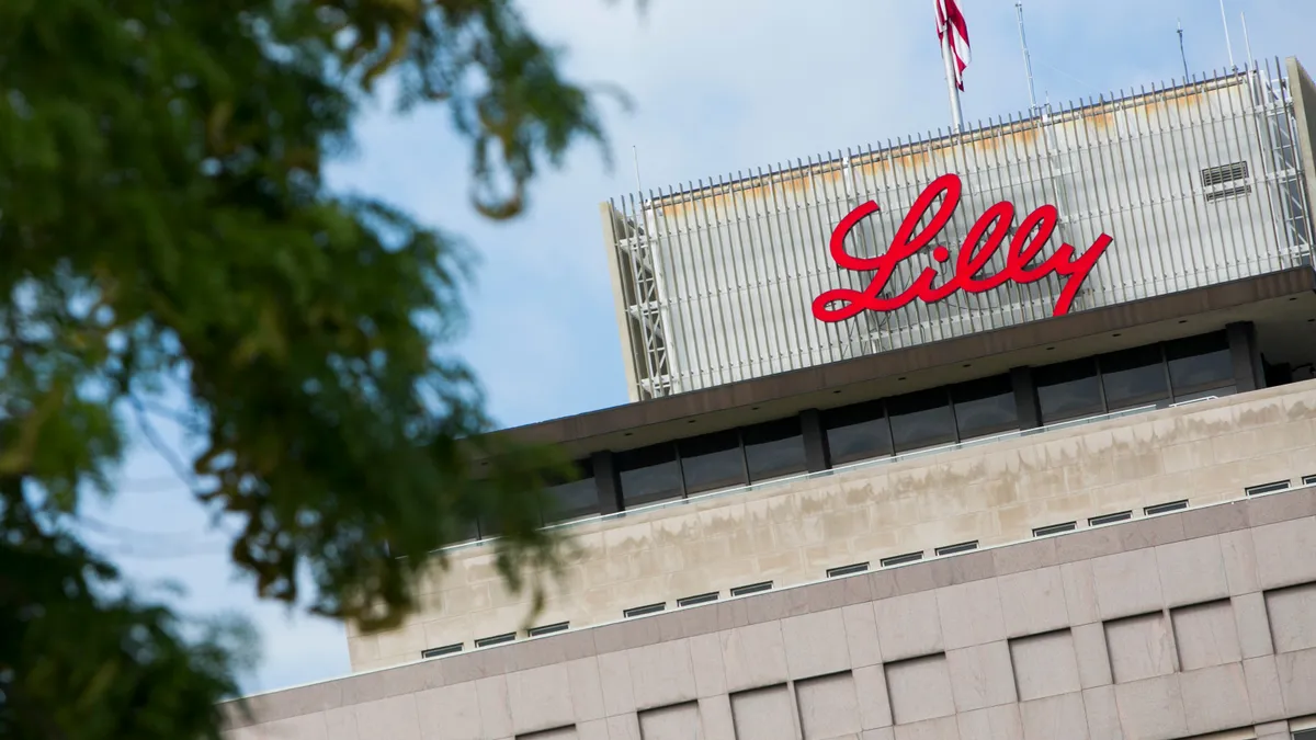 A building framed through tree foliage is seen with a sign that reads "Lilly."