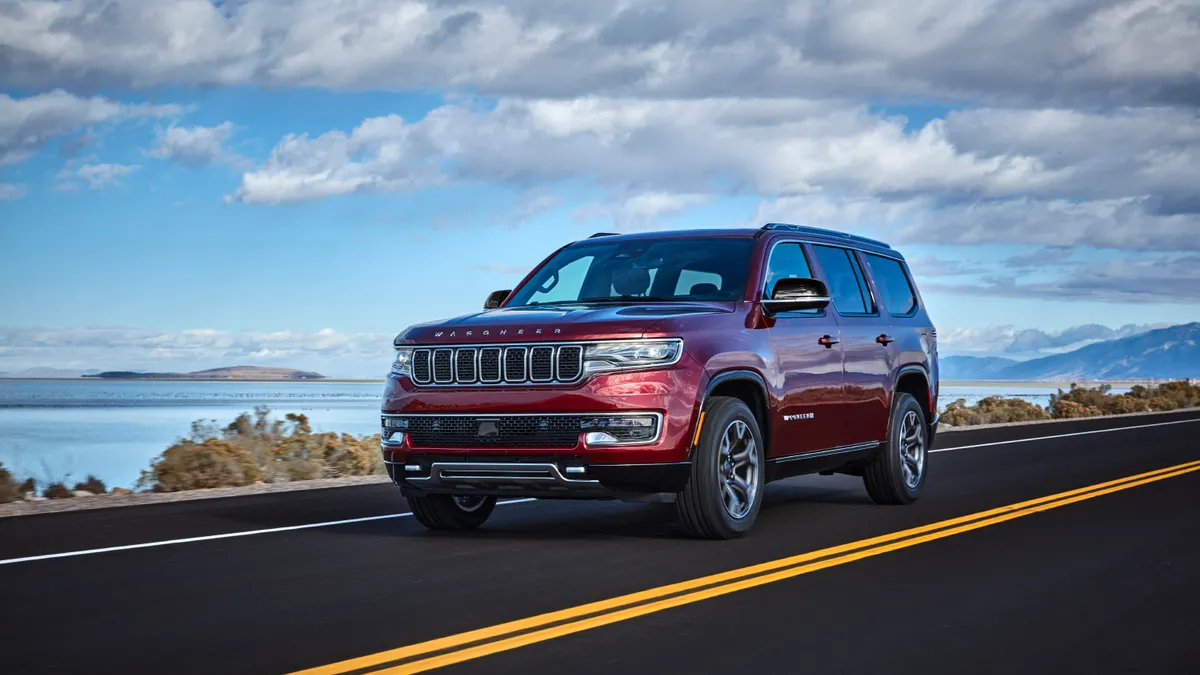 A red 2024 Jeep Wagoneer SUV driving on a highway with a body of water in the background.