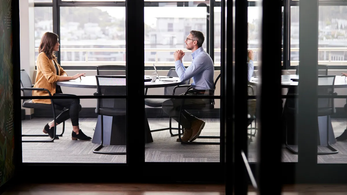 A businessman and young woman meeting for a job interview, full length, seen through glass wall